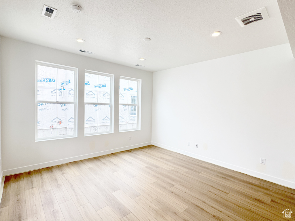 Empty room with baseboards, a textured ceiling, visible vents, and light wood-type flooring