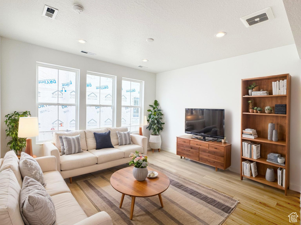 Living area with a textured ceiling, light wood-style flooring, visible vents, and recessed lighting