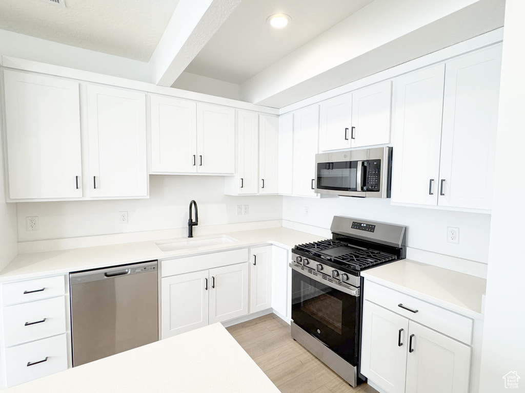 Kitchen with a sink, light wood-type flooring, appliances with stainless steel finishes, and white cabinetry