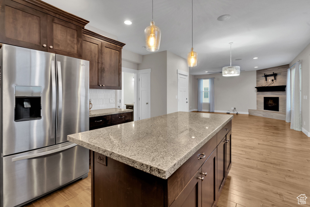 Kitchen featuring light stone counters, light hardwood / wood-style flooring, stainless steel fridge with ice dispenser, a center island, and hanging light fixtures