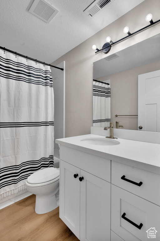 Full bathroom featuring shower / bath combo, a textured ceiling, toilet, vanity, and hardwood / wood-style flooring