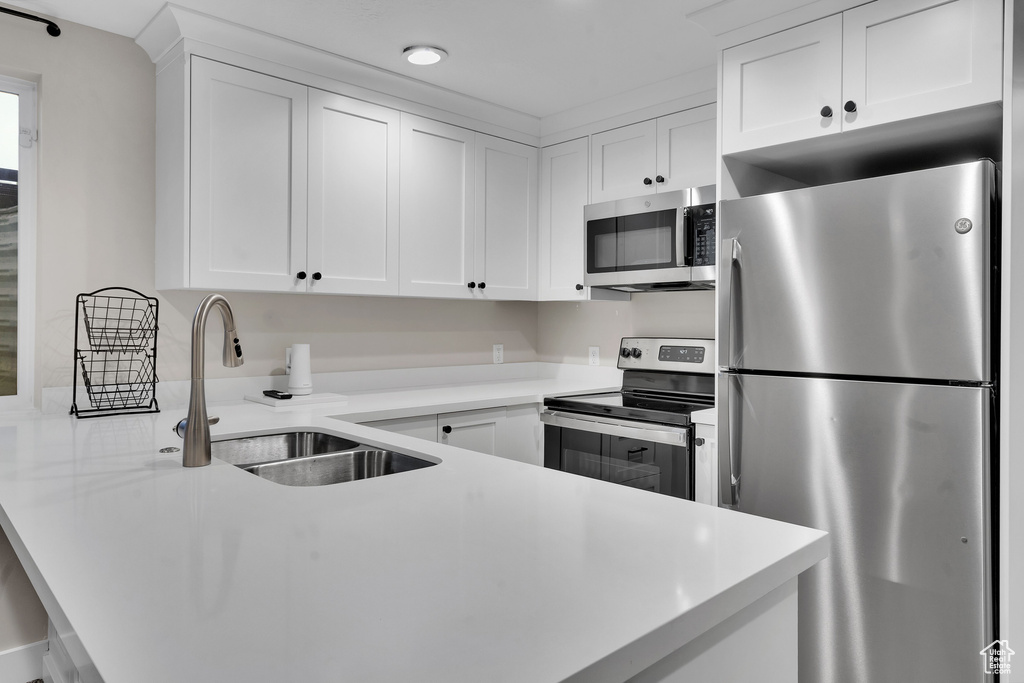 Kitchen featuring kitchen peninsula, appliances with stainless steel finishes, white cabinetry, and sink