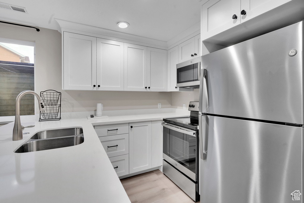 Kitchen with white cabinetry, sink, light hardwood / wood-style flooring, and appliances with stainless steel finishes