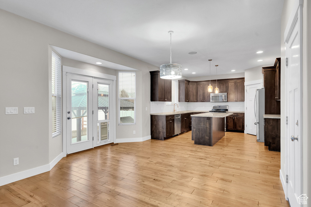 Kitchen featuring dark brown cabinetry, hanging light fixtures, stainless steel appliances, light hardwood / wood-style floors, and a kitchen island