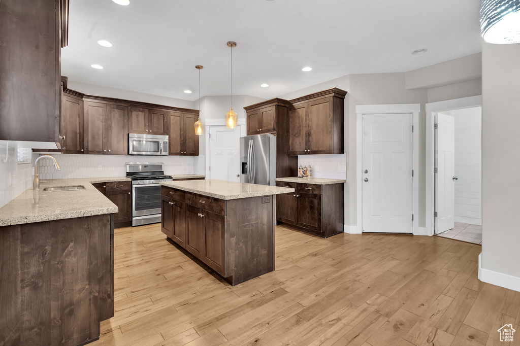 Kitchen featuring light wood-type flooring, stainless steel appliances, sink, pendant lighting, and a center island
