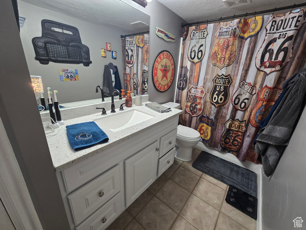 Bathroom with tile patterned flooring, vanity, toilet, a textured ceiling, and visible vents