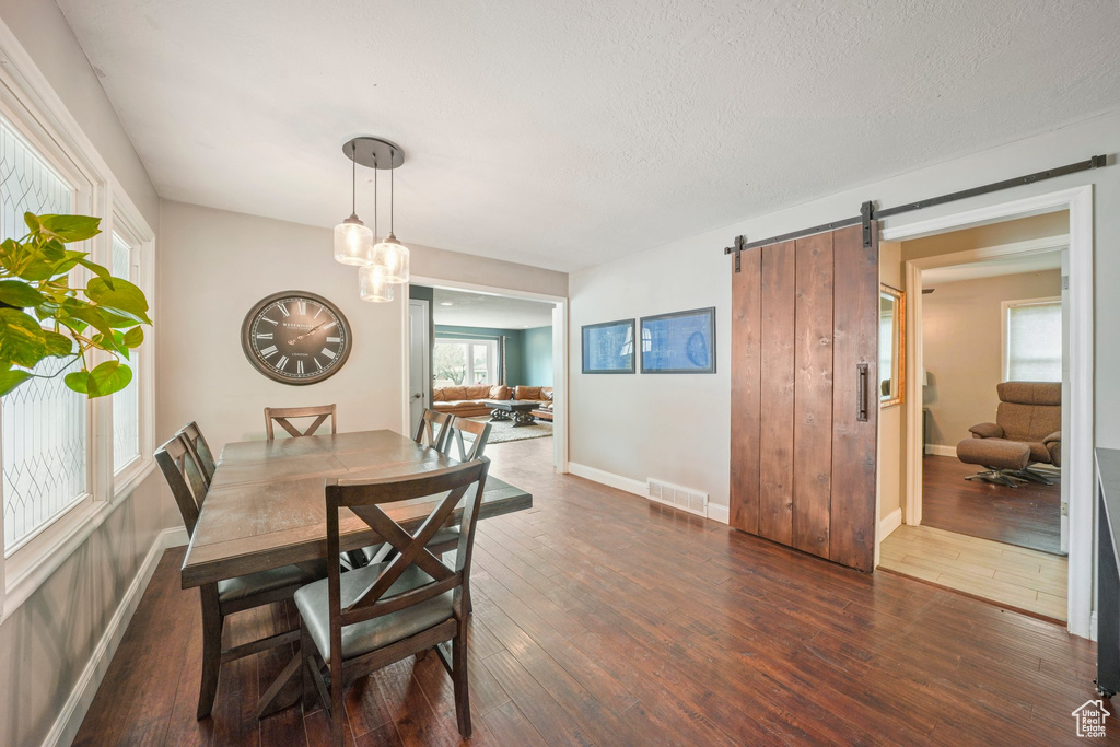 Dining room with visible vents, a textured ceiling, a barn door, wood-type flooring, and baseboards