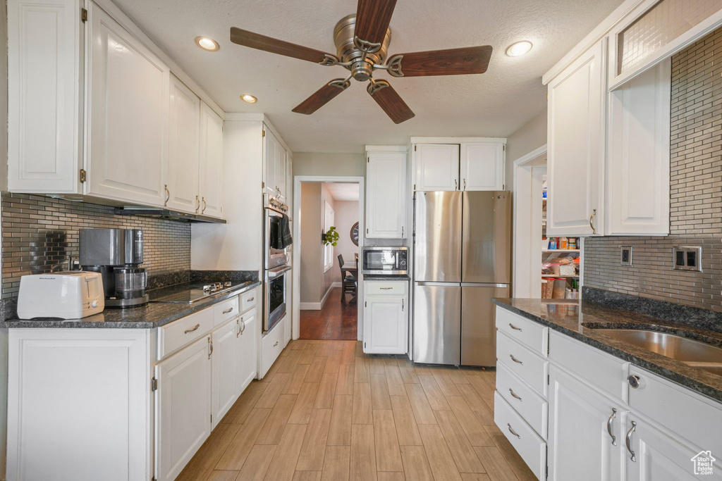 Kitchen with a ceiling fan, a sink, stainless steel appliances, white cabinetry, and light wood-type flooring