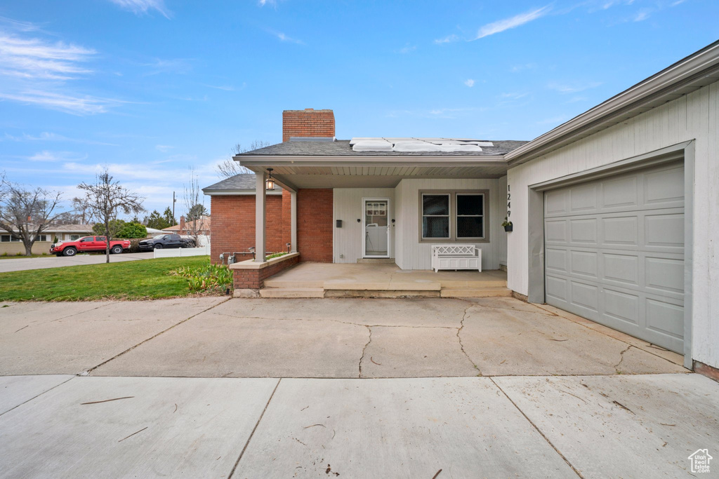 Single story home with roof mounted solar panels, covered porch, concrete driveway, a garage, and a chimney