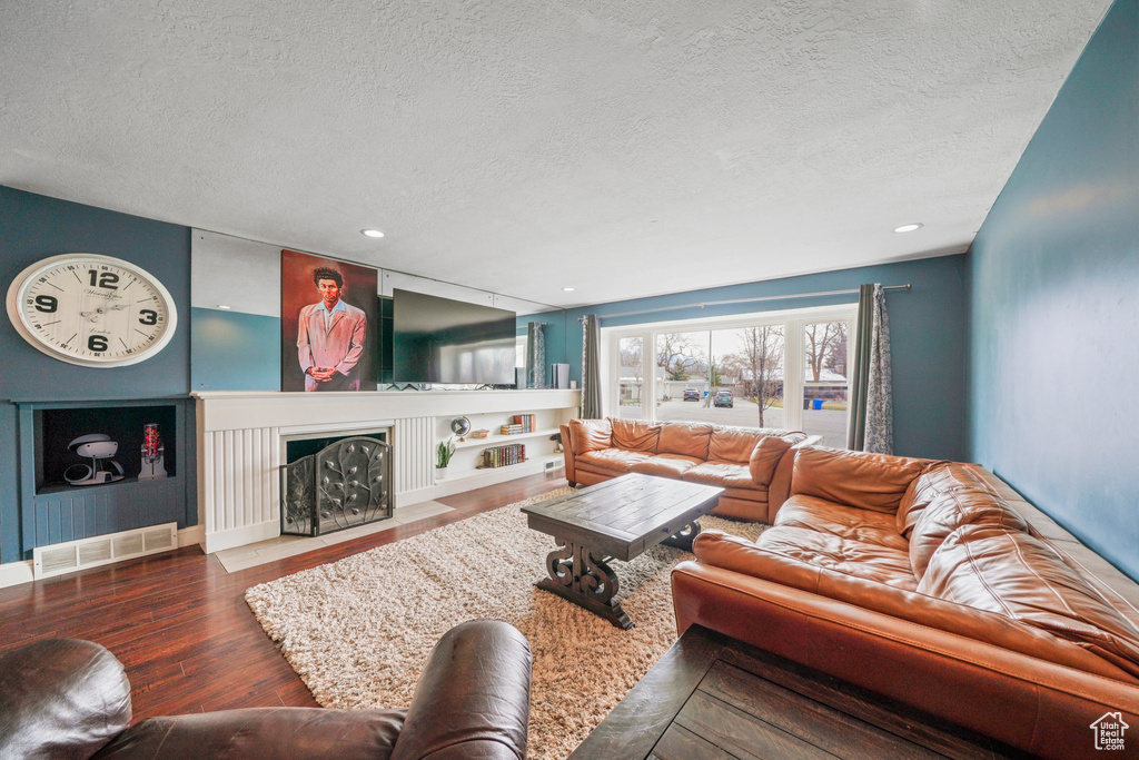 Living room with visible vents, a fireplace with flush hearth, a textured ceiling, and wood finished floors