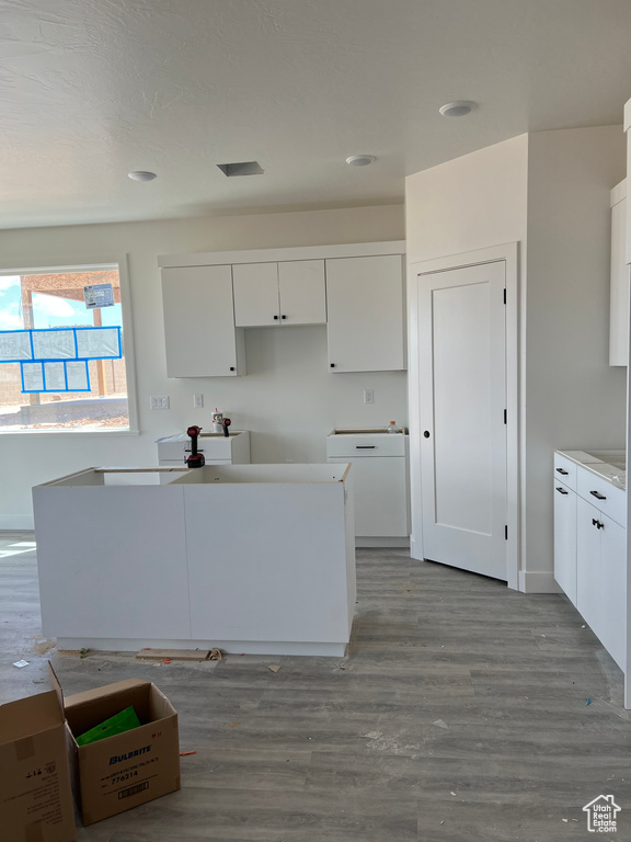 Kitchen with white cabinets, wood finished floors, a center island, and recessed lighting