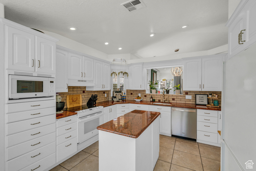 Kitchen with a sink, a kitchen island, under cabinet range hood, white appliances, and visible vents