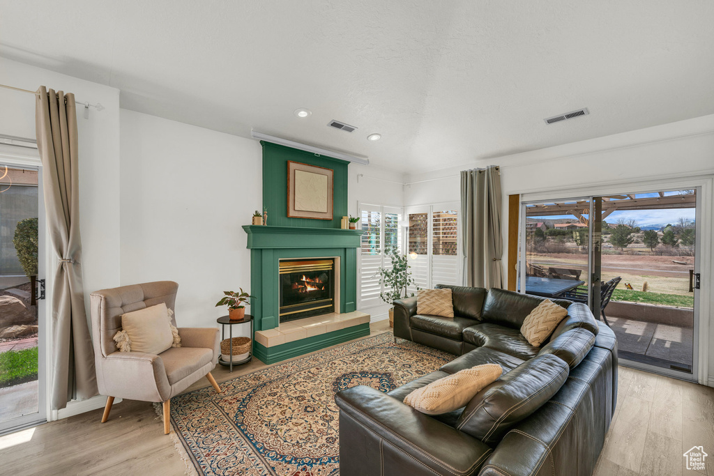Living room with visible vents, light wood-type flooring, and a glass covered fireplace