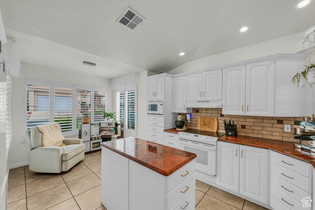 Kitchen featuring white appliances, a center island, under cabinet range hood, decorative backsplash, and visible vents
