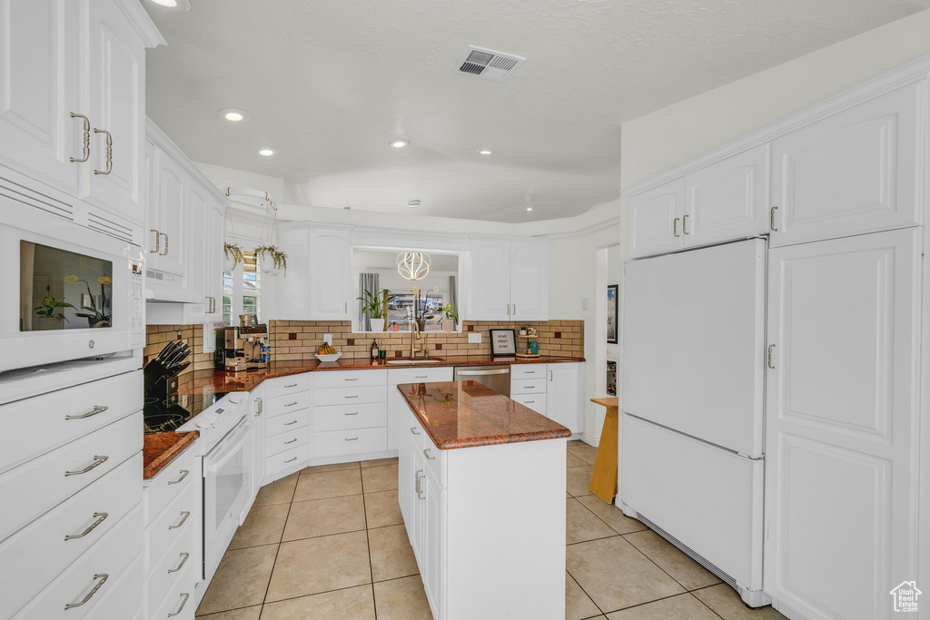 Kitchen featuring light tile patterned flooring, backsplash, a kitchen island, and white appliances