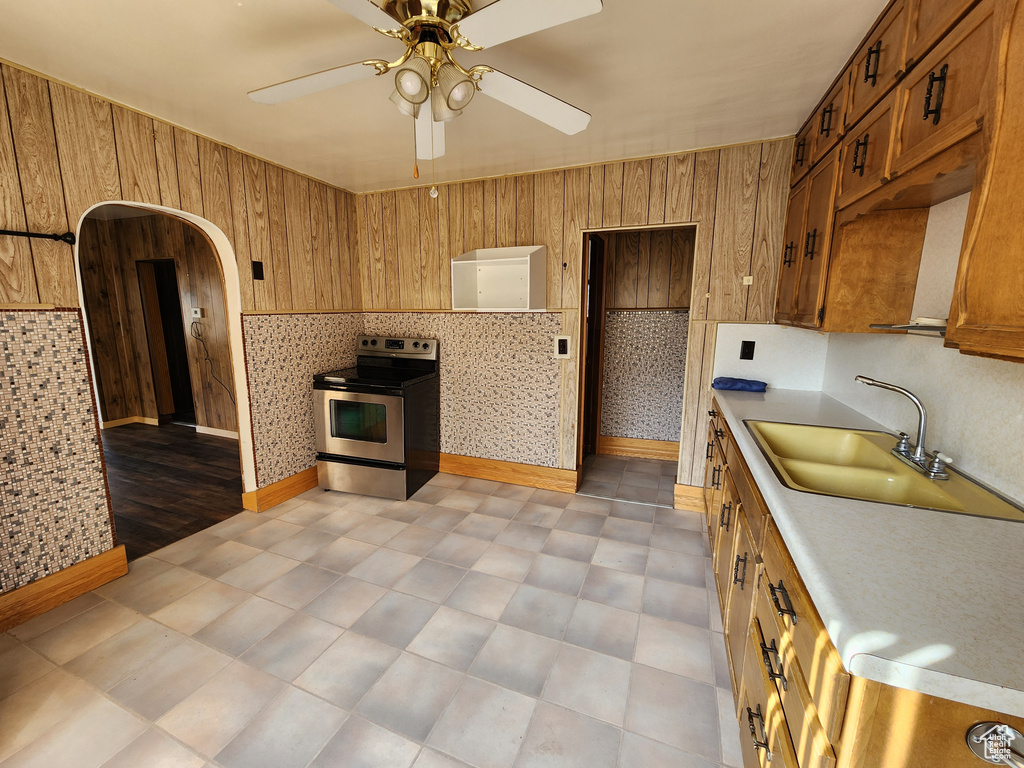 Kitchen featuring electric stove, light countertops, a ceiling fan, brown cabinetry, and a sink
