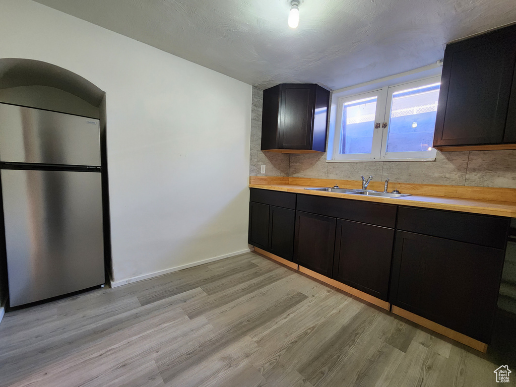 Kitchen with freestanding refrigerator, a sink, light wood-style flooring, backsplash, and dark cabinets