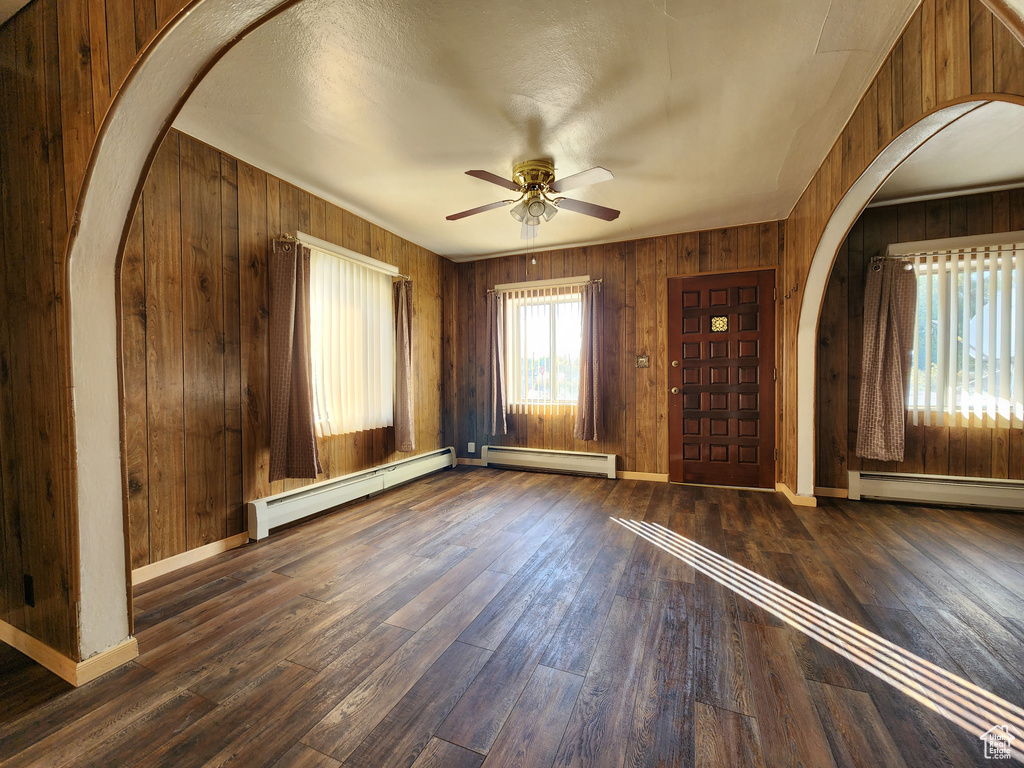 Foyer featuring baseboard heating, arched walkways, a ceiling fan, and wooden walls