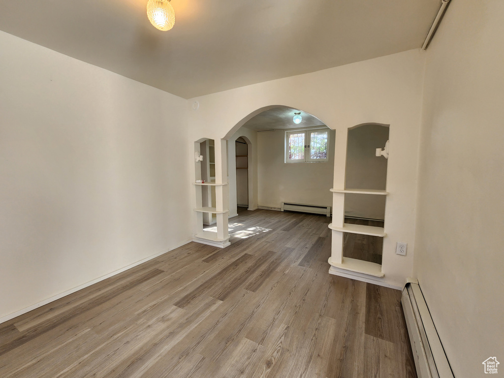 Spare room featuring baseboard heating, wood finished floors, and arched walkways