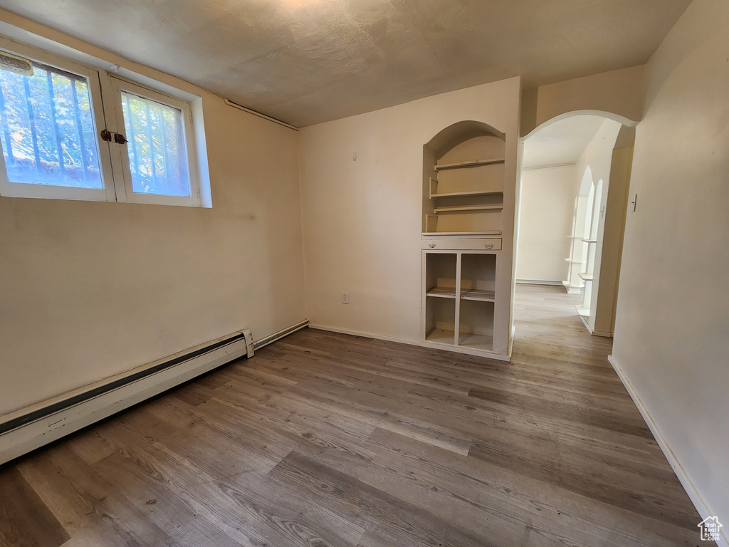 Unfurnished room with baseboard heating, arched walkways, wood finished floors, and baseboards