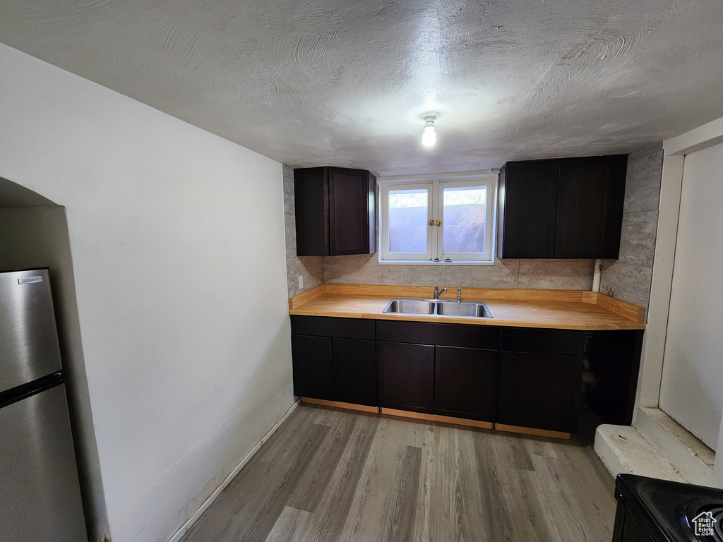 Kitchen featuring a sink, freestanding refrigerator, light wood-style flooring, light countertops, and baseboards