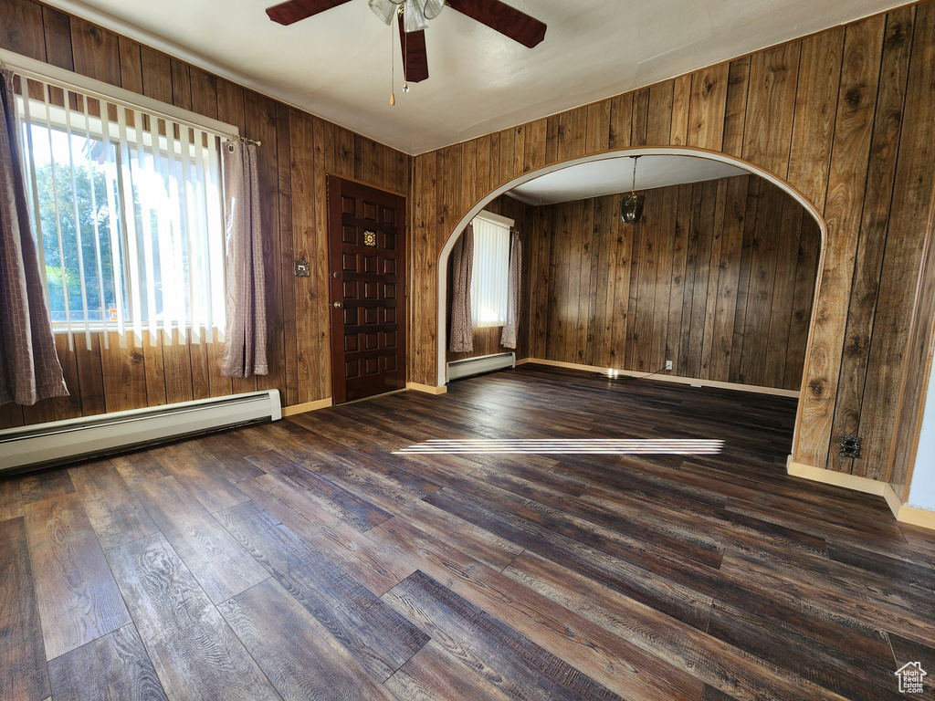 Empty room with a baseboard radiator, arched walkways, wood walls, ceiling fan, and wood finished floors
