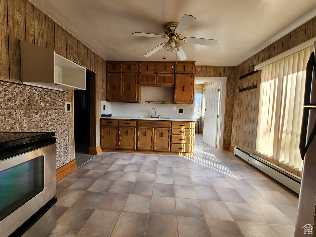 Kitchen with stainless steel range with electric stovetop, a baseboard radiator, wooden walls, light countertops, and ceiling fan