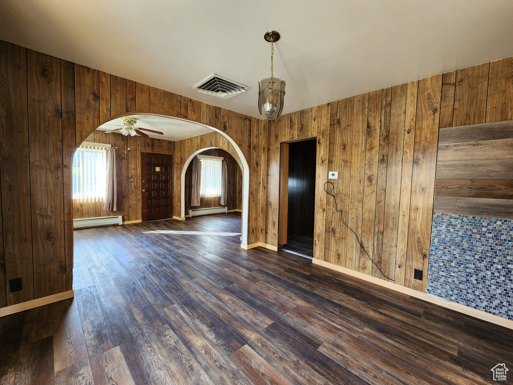 Unfurnished room featuring arched walkways, a baseboard radiator, wooden walls, dark wood-style floors, and baseboards