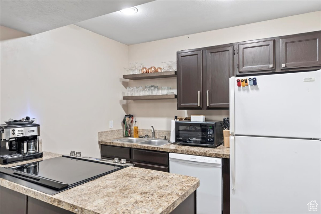 Kitchen featuring light countertops, white appliances, dark brown cabinetry, a sink, and open shelves