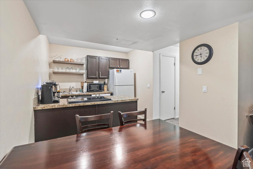 Kitchen with open shelves, a peninsula, light stone countertops, dark brown cabinetry, and black appliances