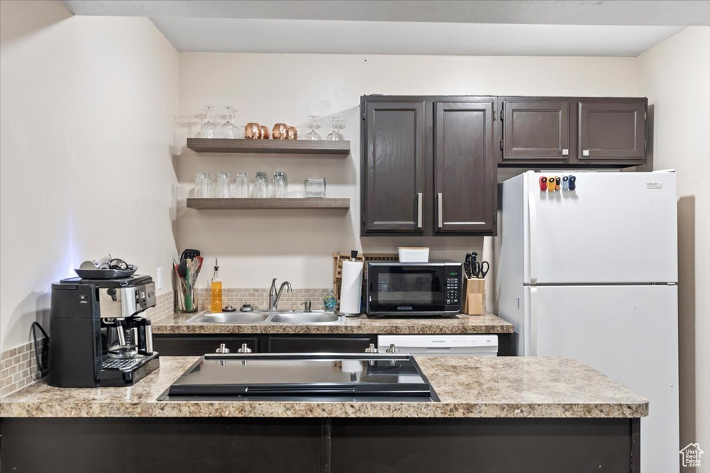 Kitchen with light countertops, dark brown cabinetry, a sink, a peninsula, and white appliances
