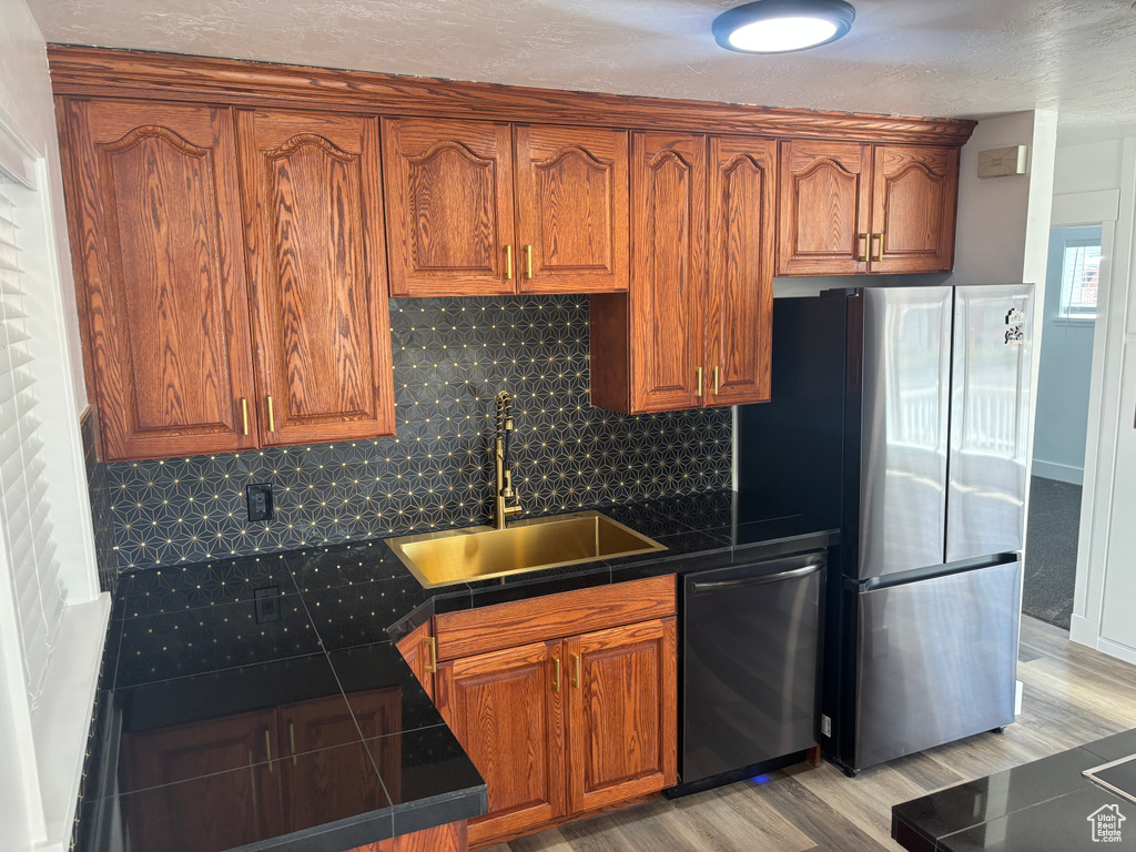 Kitchen with decorative backsplash, a sink, light wood-style floors, appliances with stainless steel finishes, and brown cabinetry