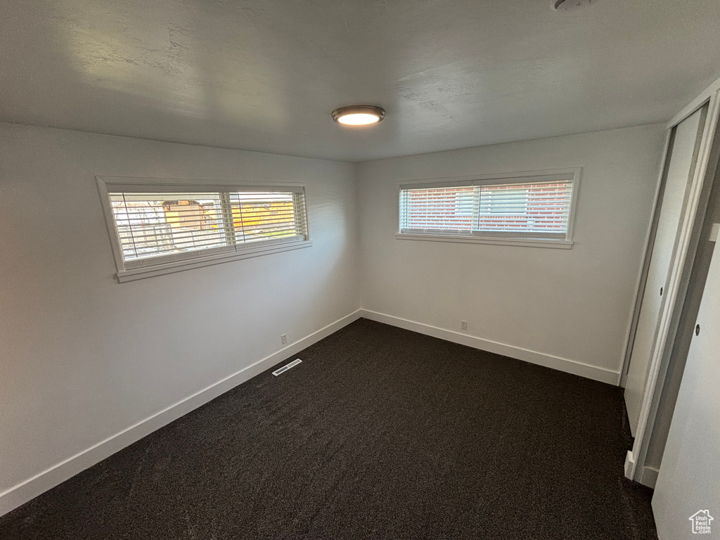 Unfurnished bedroom with baseboards, dark carpet, and visible vents