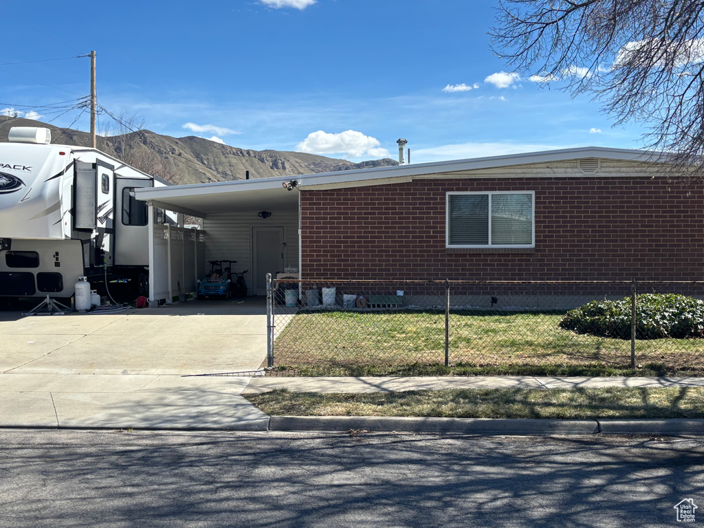 View of front of home with concrete driveway, an attached carport, brick siding, a fenced front yard, and a mountain view