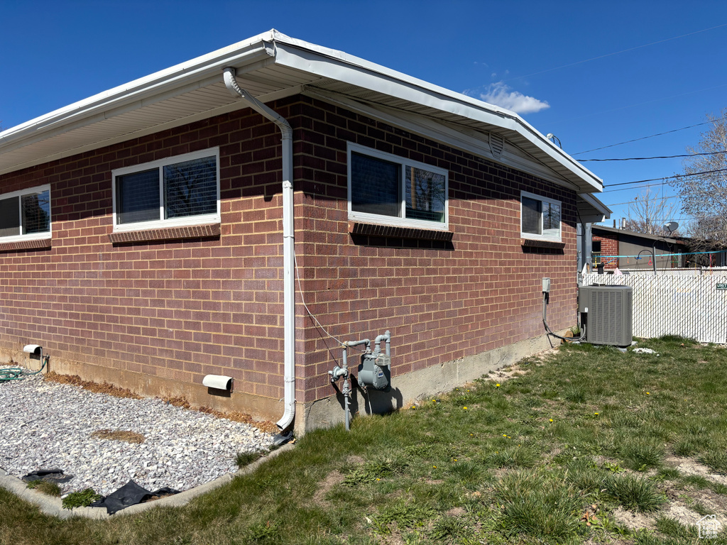 View of side of property featuring fence, crawl space, central AC unit, brick siding, and a lawn