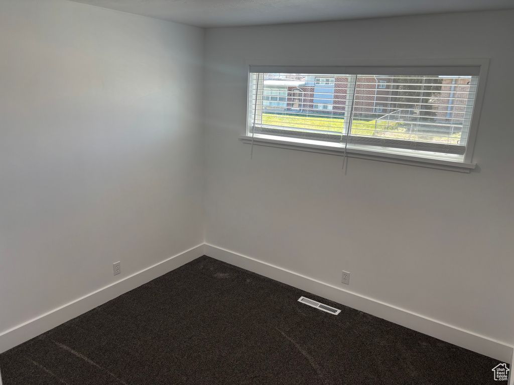 Spare room with baseboards, visible vents, and dark carpet