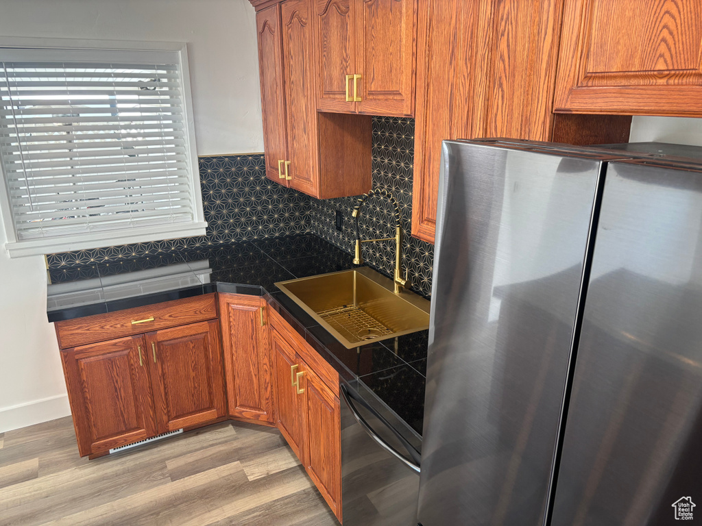 Kitchen with a sink, dishwashing machine, light wood-type flooring, brown cabinetry, and freestanding refrigerator