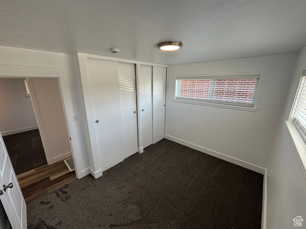 Unfurnished bedroom featuring dark carpet, a closet, baseboards, and a textured ceiling