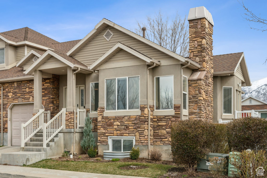 View of front facade featuring stone siding, stucco siding, roof with shingles, and a chimney