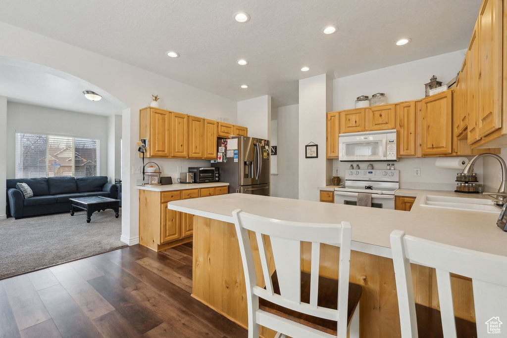 Kitchen with light countertops, white appliances, a sink, arched walkways, and a peninsula