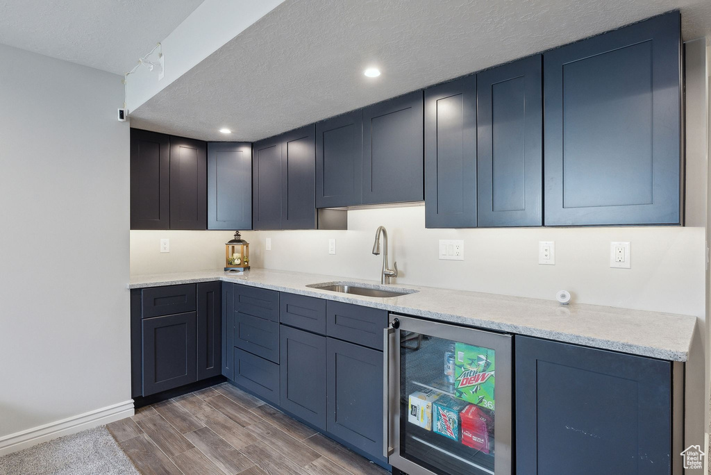 Kitchen featuring light countertops, wine cooler, a textured ceiling, a sink, and light wood finished floors
