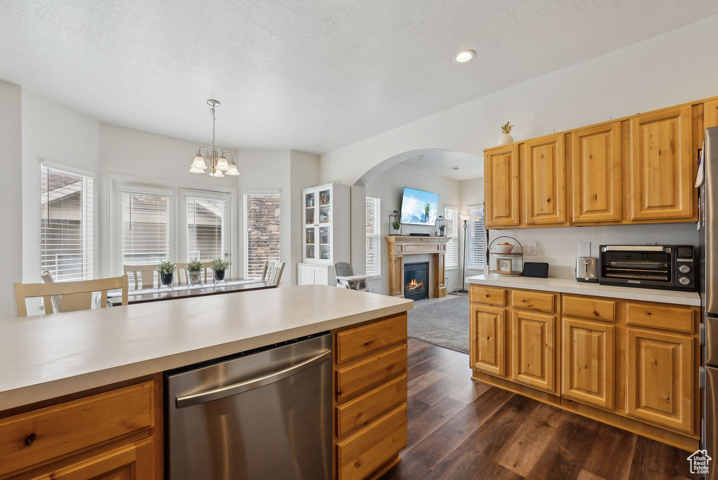 Kitchen with light countertops, stainless steel dishwasher, dark wood-style floors, arched walkways, and an inviting chandelier
