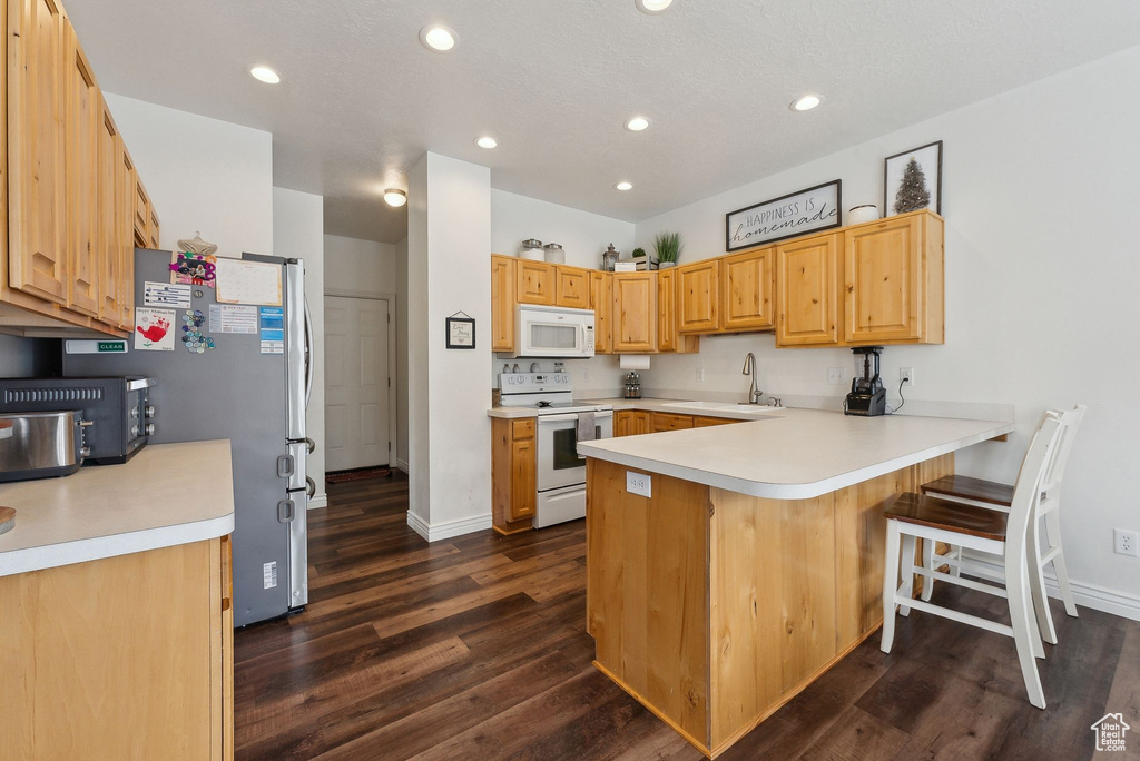 Kitchen featuring a sink, a peninsula, dark wood-style floors, white appliances, and recessed lighting