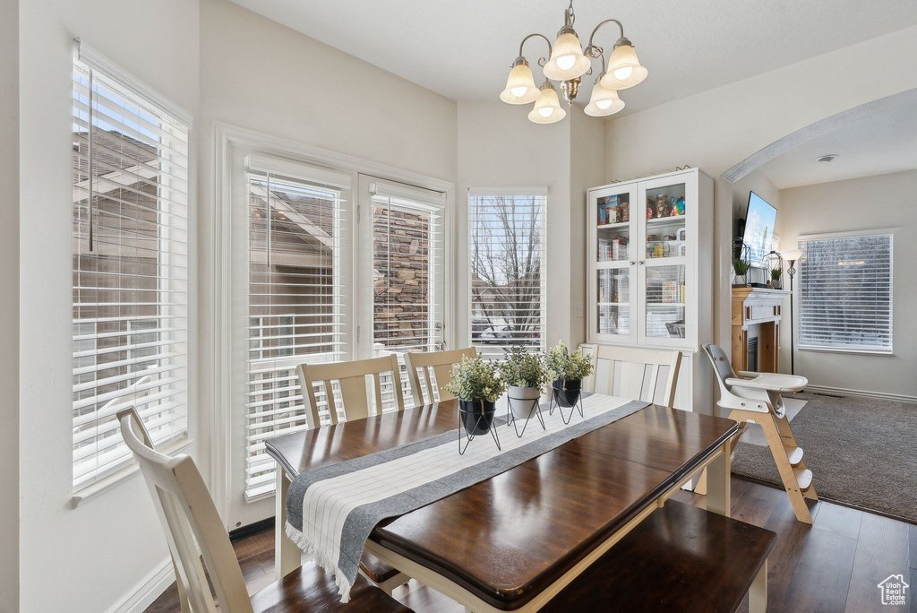 Dining space with an inviting chandelier, arched walkways, a healthy amount of sunlight, and wood finished floors