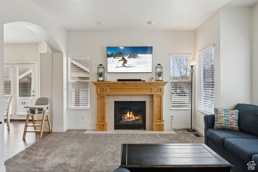 Living room with carpet flooring, arched walkways, a tile fireplace, and baseboards