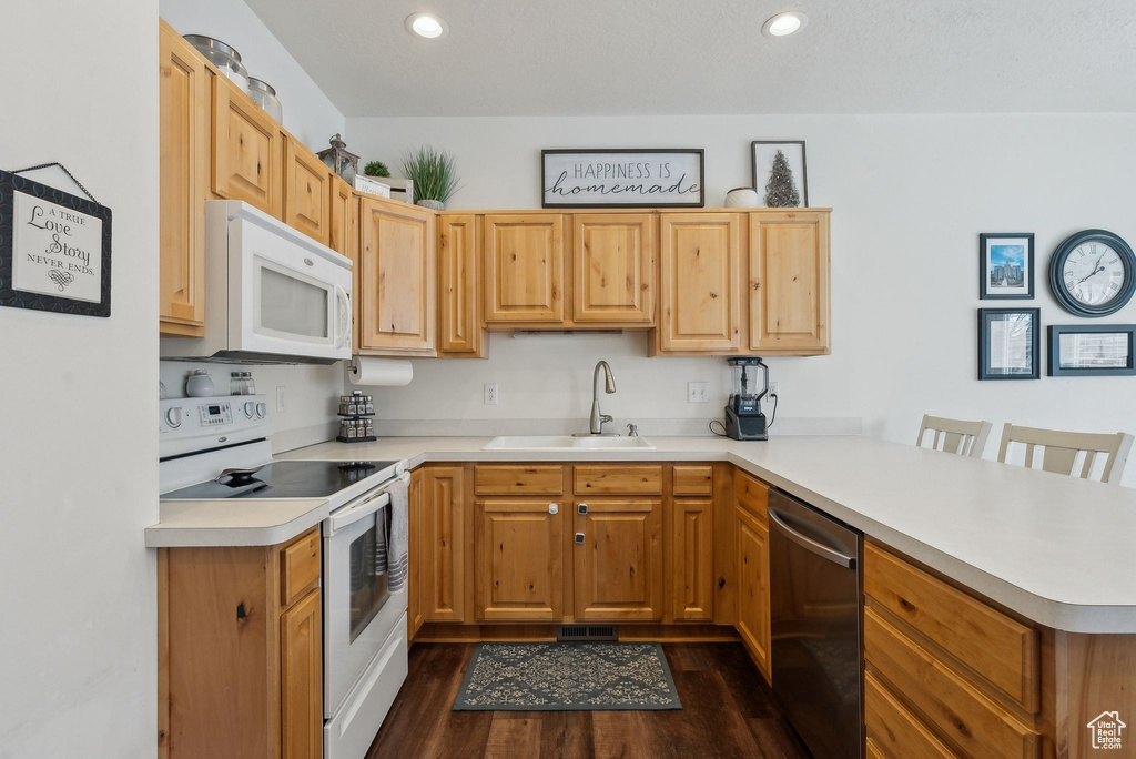 Kitchen featuring light countertops, a sink, a peninsula, white appliances, and dark wood-style flooring