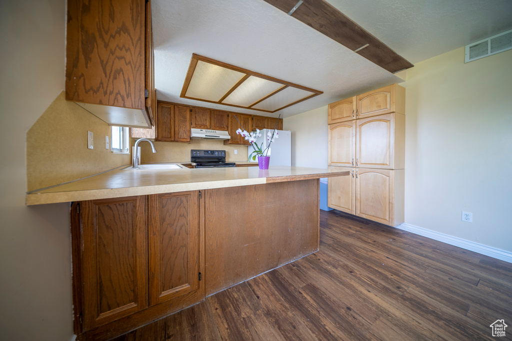 Kitchen with a sink, freestanding refrigerator, a peninsula, under cabinet range hood, and range with electric stovetop