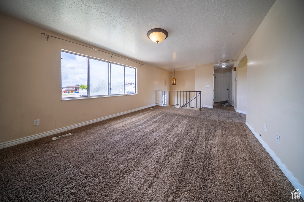 Carpeted empty room with visible vents, a textured ceiling, and baseboards