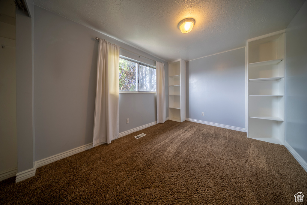 Carpeted empty room featuring baseboards, a textured ceiling, and visible vents