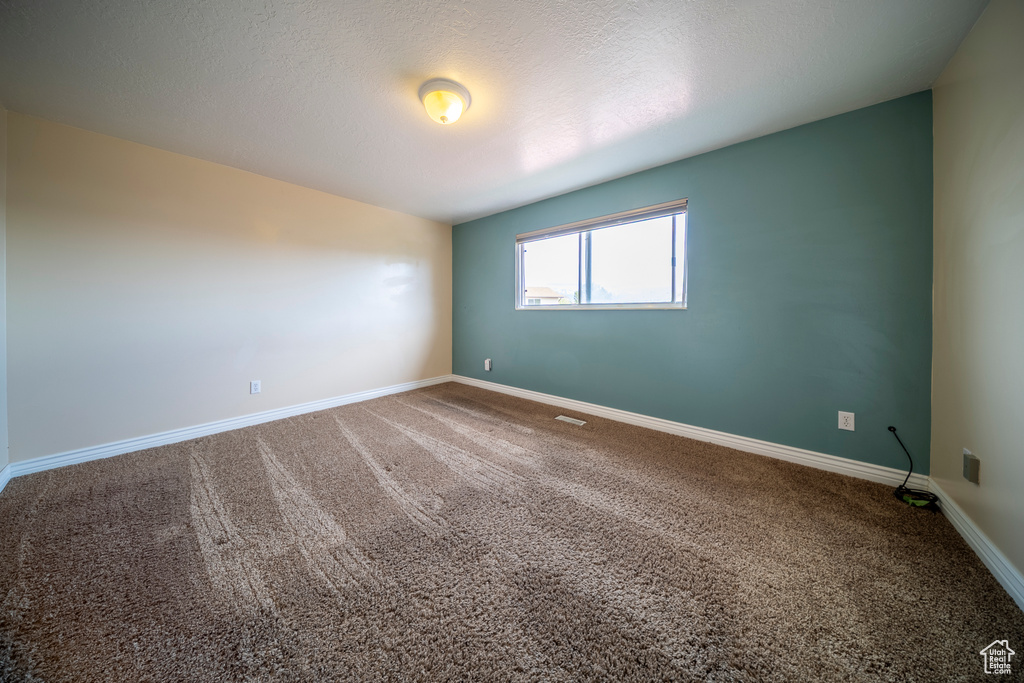 Empty room featuring carpet flooring, a textured ceiling, baseboards, and visible vents